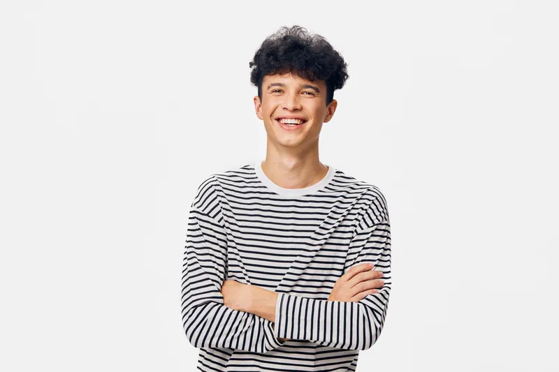 smiling man wearing striped long sleeve shirt with crossed arms, curly hair, casual look, isolated on white background, cheerful expression