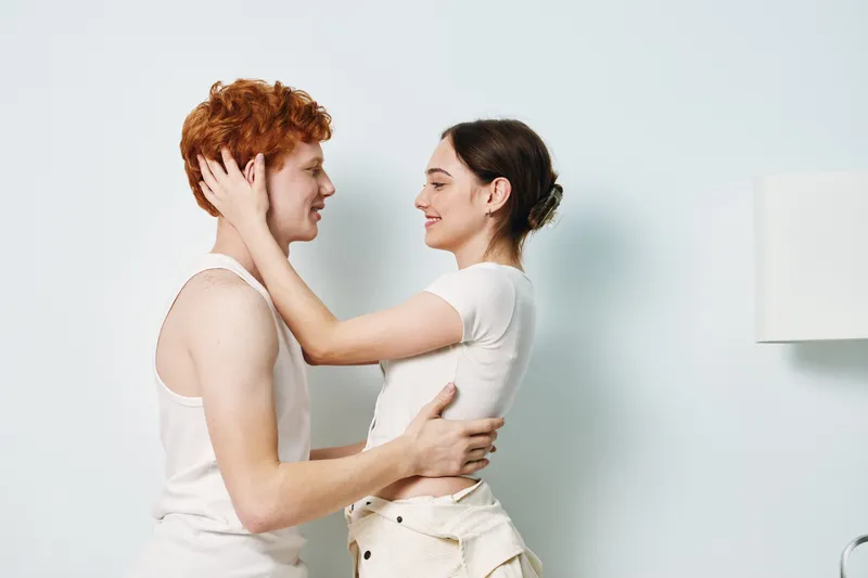 Young couple hugging and smiling at home in casual clothes, intimacy and love with tenderness and happiness in relationship, light background and relaxed mood.