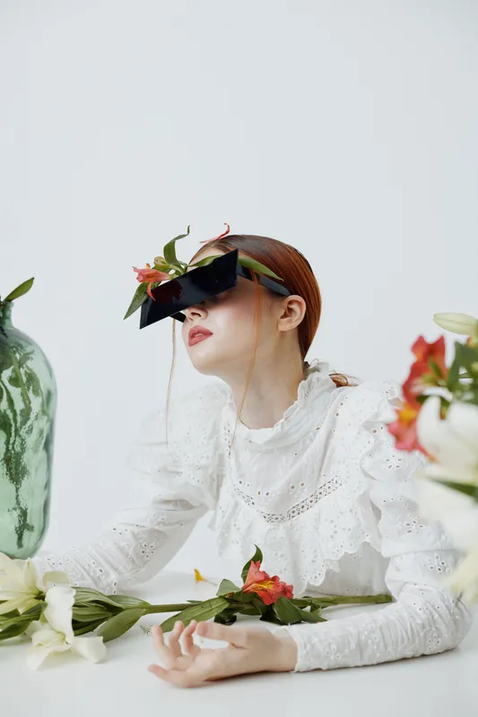 Stylish young woman with floral sunglasses in a minimalistic setting, showcasing beauty and fashion with a delicate touch of nature and elegance