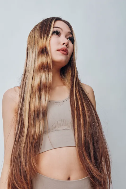Young woman with long straight hair wearing beige crop top looking up, beauty and fashion portrait with natural makeup on white background for haircare and style.