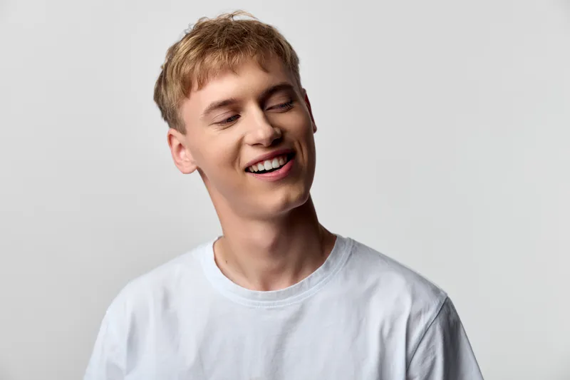 Smiling man in a white tshirt stands against a neutral backdrop, exuding casual style, positive energy and everyday ease, capturing a candid moment of joy and approachable friendliness