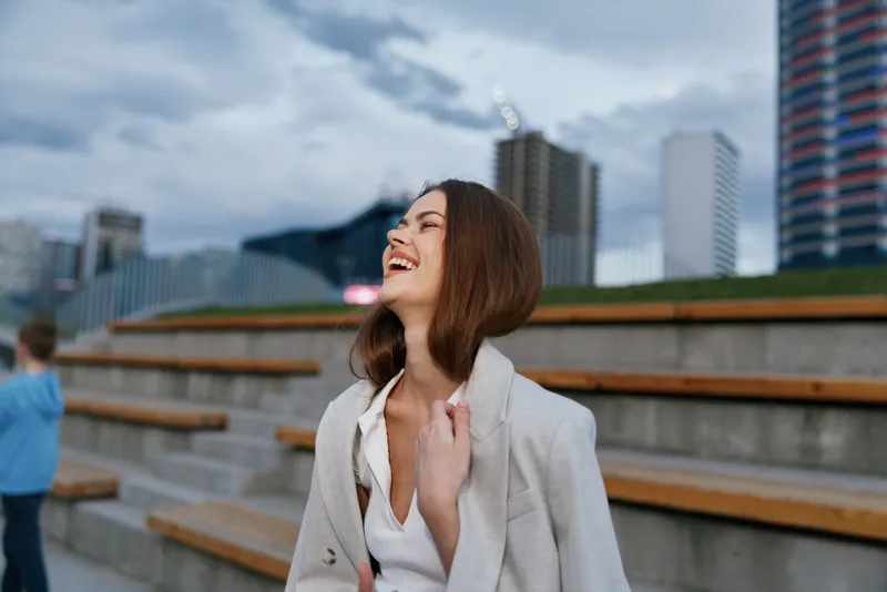 Woman laughing in white blouse and light coat outdoors urban background smiling happy positive emotion business fashion