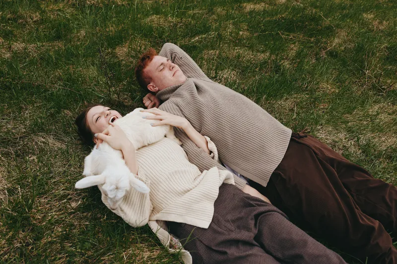 Couple lying on grass outdoors, wrapped in sweater, relaxed, cozy, lifestyle, portrait, leisure, nature, calm, serene, warmth, smiles, together, companionship, sunshine, breeze, comfort, harmony,