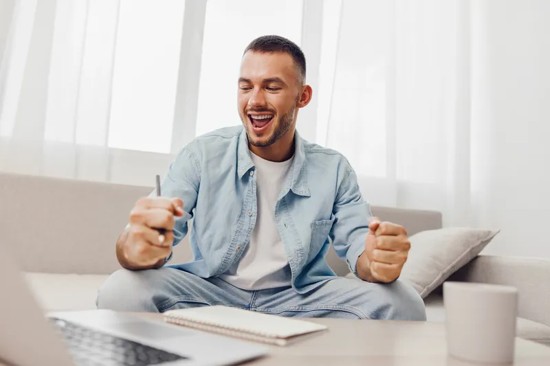Excited man celebrating success while working from home, dressed casually in denim and relaxed environment. Inspired mood enhances the joy of productivity.