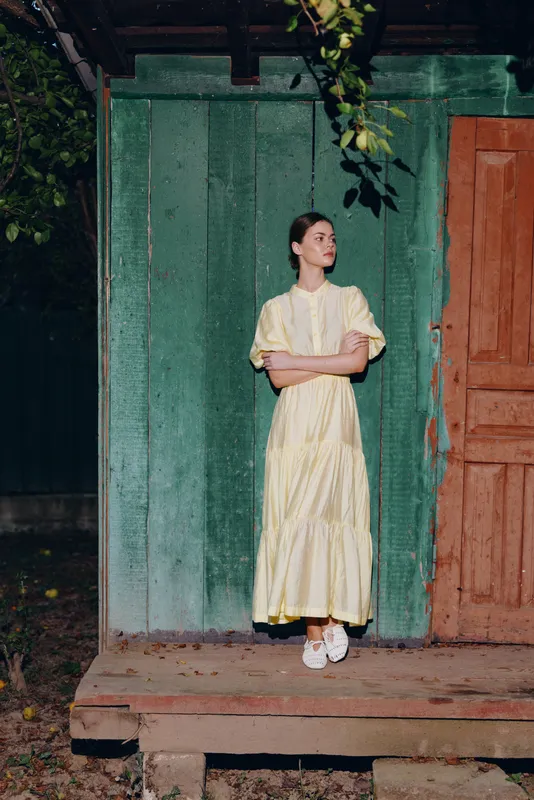 Woman in yellow dress on wooden porch against green wall calm light authentic inclusive