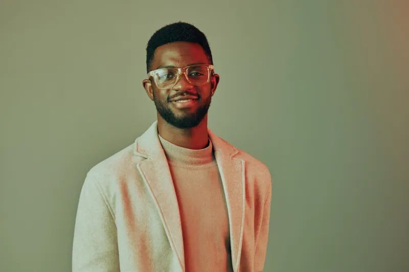 Stylish young African man with glasses in a beige blazer against a gray background, exuding confidence and positivity, perfect for fashion and lifestyle themes