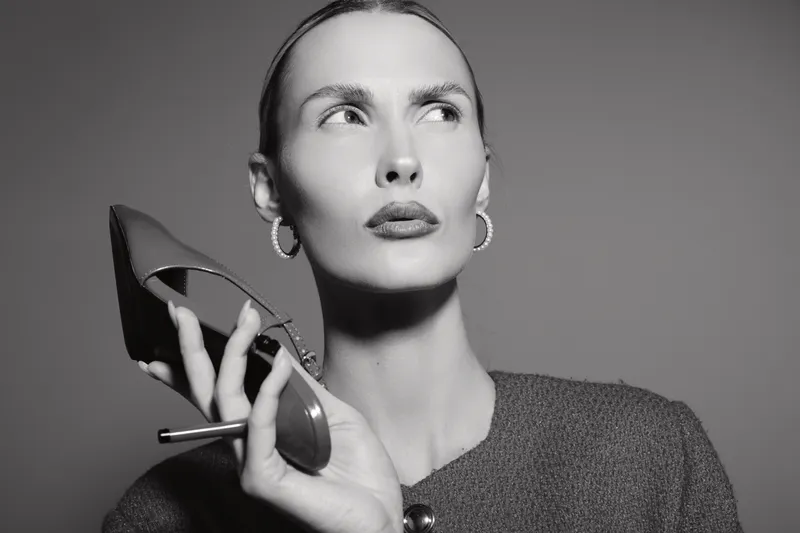 Portrait of a fair skinned Caucasian woman holding a shoe near her face looking away. Studio black and white photo with elegant fashion and beauty concept.