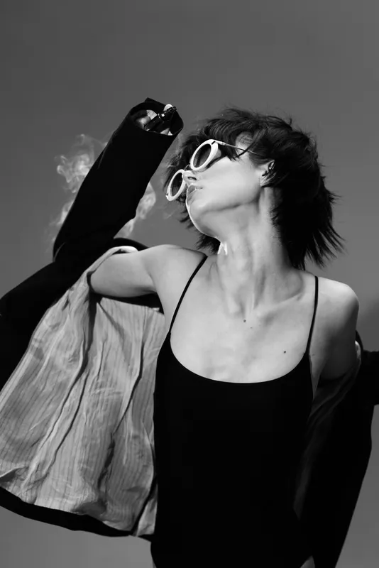 Black and white portrait of a stylish woman dancing with sunglasses and a jacket in motion.