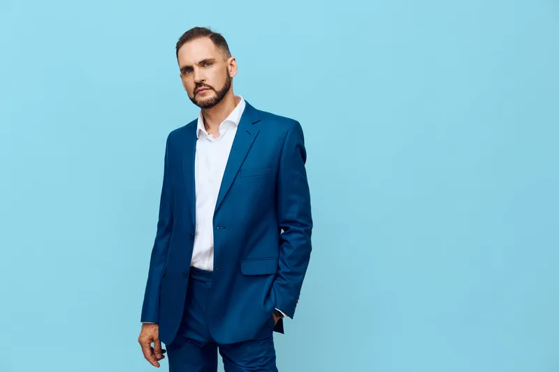 A professional man in a tailored blue suit stands against an isolated blue background, projecting confidence, calm focus, and poised emotion suitable for corporate media and leadership contexts.
