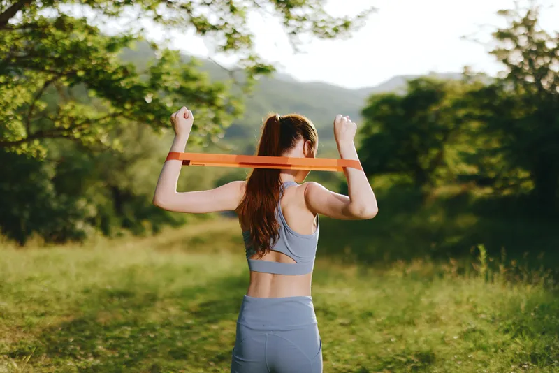 Young woman practicing outdoor stretching with resistance band, showcasing athletic wear, nature background, vibrant colors, emphasizing fitness and healthy lifestyle