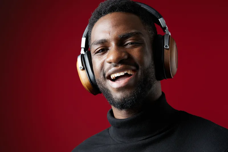 Happy young man wearing stylish headphones against a vibrant red background, showcasing an upbeat emotion while enjoying music