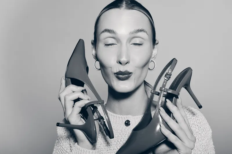 Young white woman with light skin holding high heel shoes close to face with closed eyes. Concept for fashion accessories, style, and elegant footwear in studio.