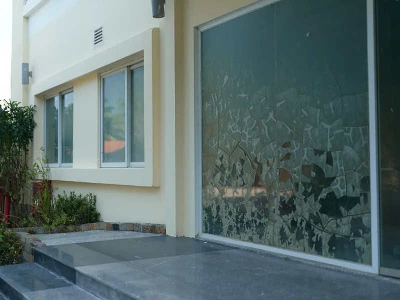 Modern house exterior with large glass window featuring decorative frosted patterns, stone steps leading to entrance, and surrounding greenery in daylight