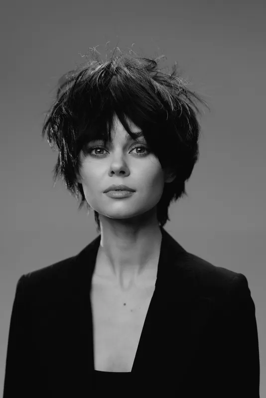 Black and white portrait of a young woman with short messy hair wearing a dark blazer with a neutral expression