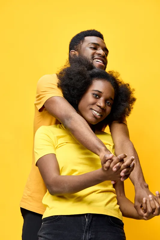 A joyful couple embracing against a vibrant yellow background, wearing matching yellow T shirts, portraying happiness and love in a sunny, cheerful atmosphere