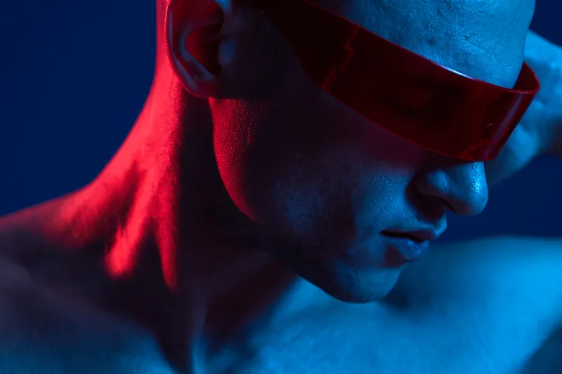 Profile of a man wearing red sunglasses, showcasing unique lighting and colors that create a striking visual contrast. The image captures an edgy, modern vibe.