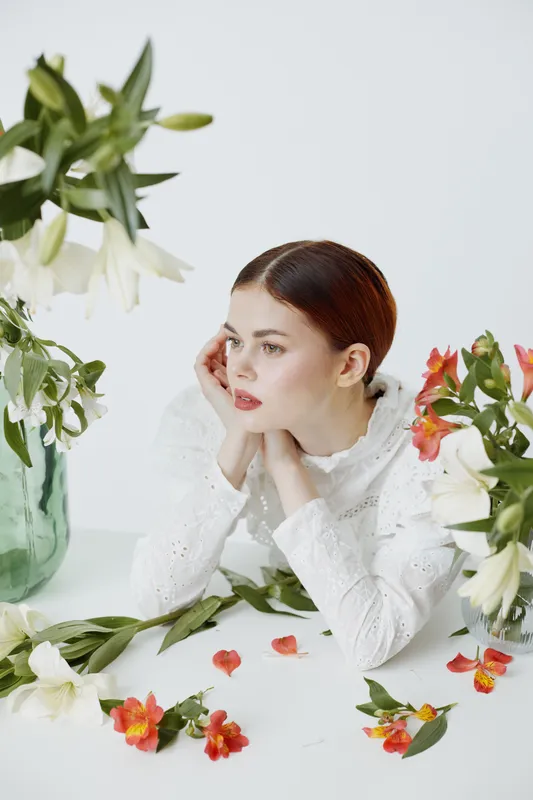 Elegant young woman in white blouse surrounded by colorful flowers, showcasing spring beauty and tranquility, with soft emotions and a fresh atmosphere