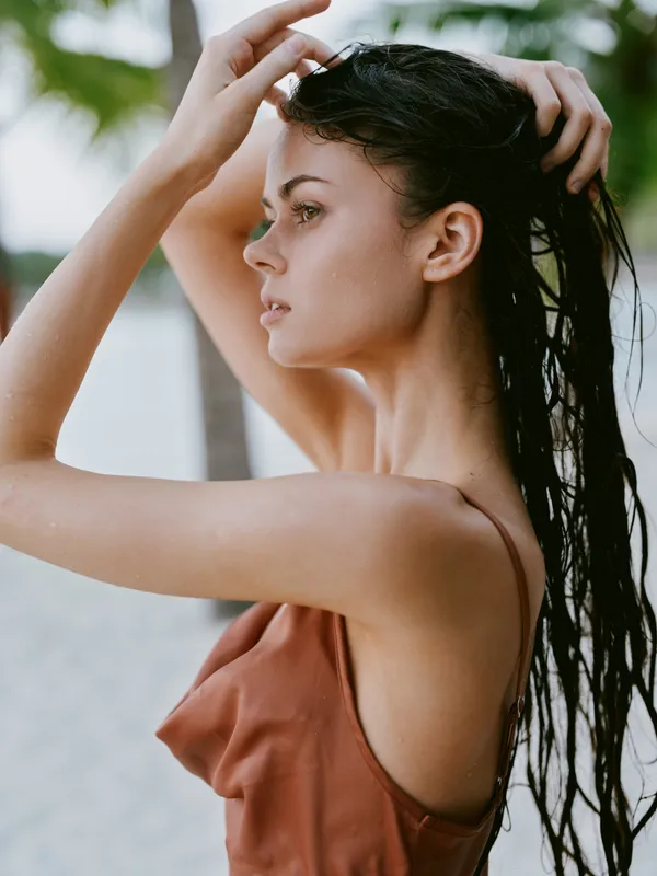 Side portrait of a woman with wet hair on a beach, wearing a brown sleeveless top. Soft light, calm expression, water droplets on skin, natural beauty, sunny summer mood.
