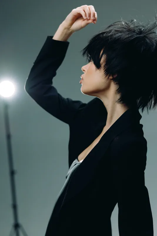 Profile of a stylish woman with short black hair posing against a dark background with studio lighting.
