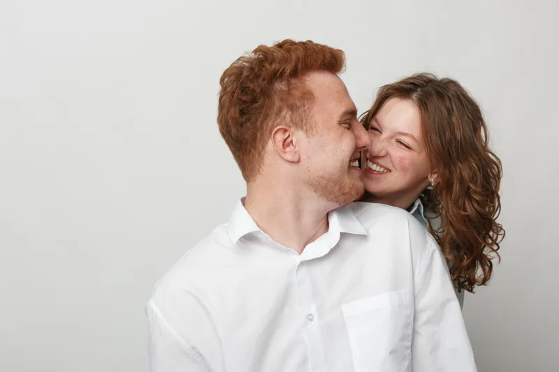 Happy young couple with red hair and curly hair smiling and embracing each other on white background. Concept of love, affection, relationship, and joyful moments together.