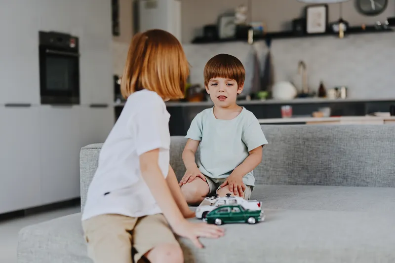 Two children playing together, one boy and one girl, enjoying quality time at home in a cozy, bright living room with colorful toys around.
