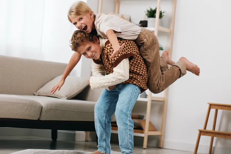 Authentic moment of playful family life, a child riding on a father's back during a lively indoor game, conveying joy, warmth, and genuine everyday connection.