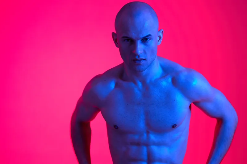 Strong man posing in vibrant blue light, showcasing athletic physique. The dramatic colors create an engaging and energetic atmosphere, highlighting his defined muscles.