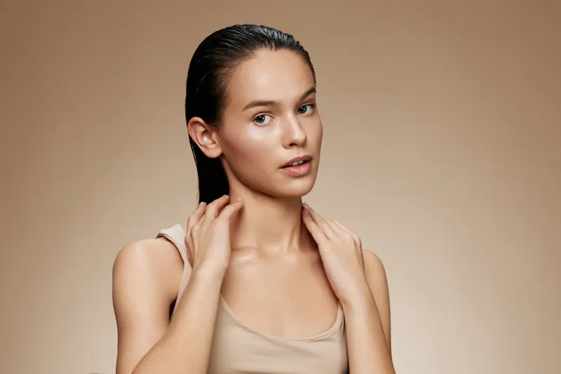 Young woman with wet hair posing against a neutral background, expressing confidence and beauty, wearing a simple beige top, showcasing natural skin tones