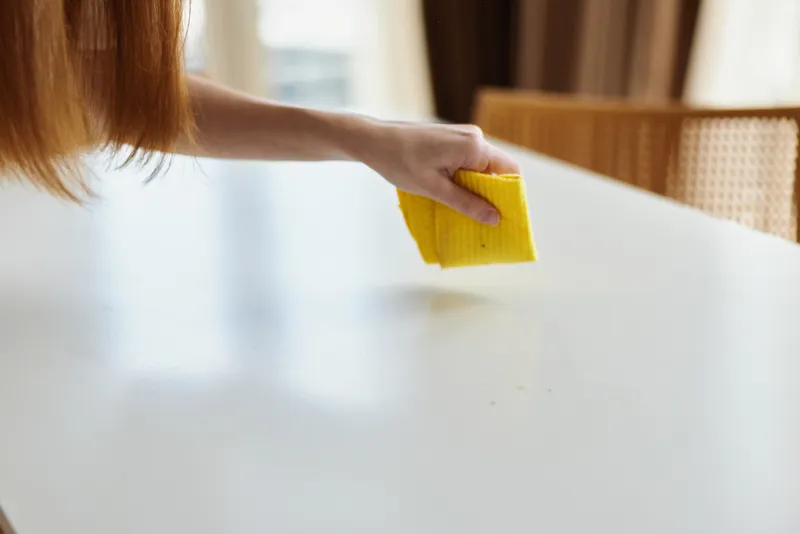 Cleaning table with yellow sponge and hand wiping white surface in bright kitchen, closeup of household chore and surface maintenance for hygiene, tidy home routine.
