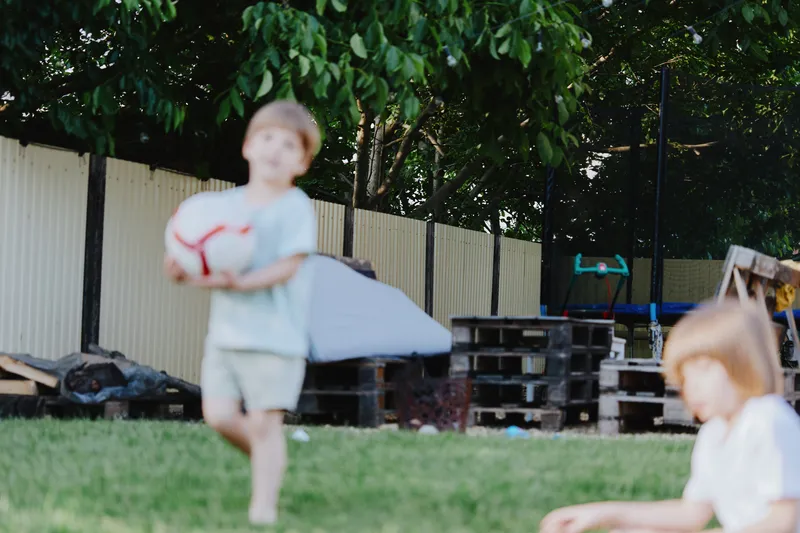 Playful boy with ball enjoying a sunny day outside, surrounded by greenery and wooden structures. Perfect for family and children's themed projects.