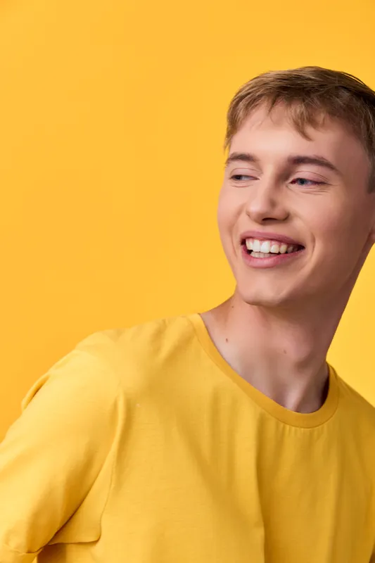 Smiling man wearing a yellow shirt stands before a bright yellow backdrop, radiating cheerful energy, modern style, and positive mood for marketing campaigns, advertising, branding