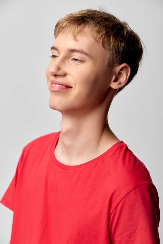 Smiling young man in a red shirt in a studio setting, casual mood, soft lighting, cheerful expression, relaxed pose, positive vibe, modern lifestyle image