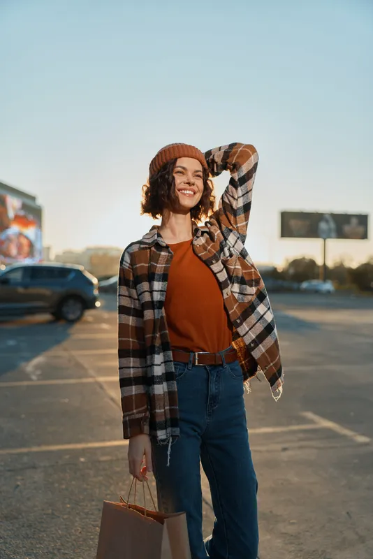 Woman smile shopping in parking at golden hour, wearing beanie and plaid jacket with jeans. Authenticity, candid lifestyle and mindful living convey emotional storytelling and warm golden glow.