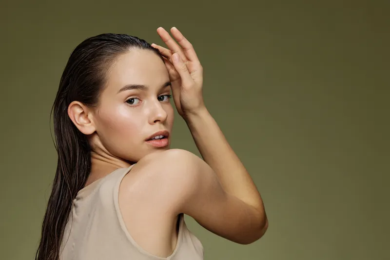 Young woman with wet hair posing gracefully against a muted green background, exuding confidence and natural beauty in a minimalistic style
