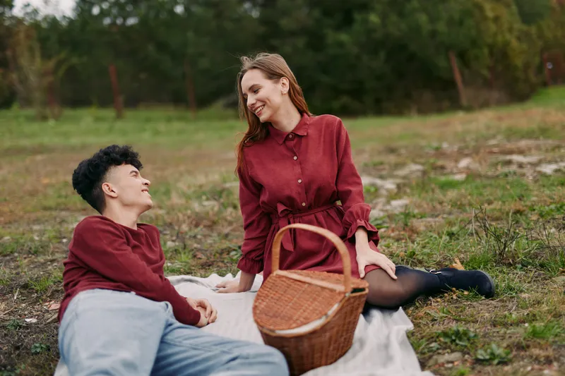 Authenticity and credibility shine in a candid outdoor moment as two friends share a quiet picnic on a field with natural light, a blanket, and a wicker basket.