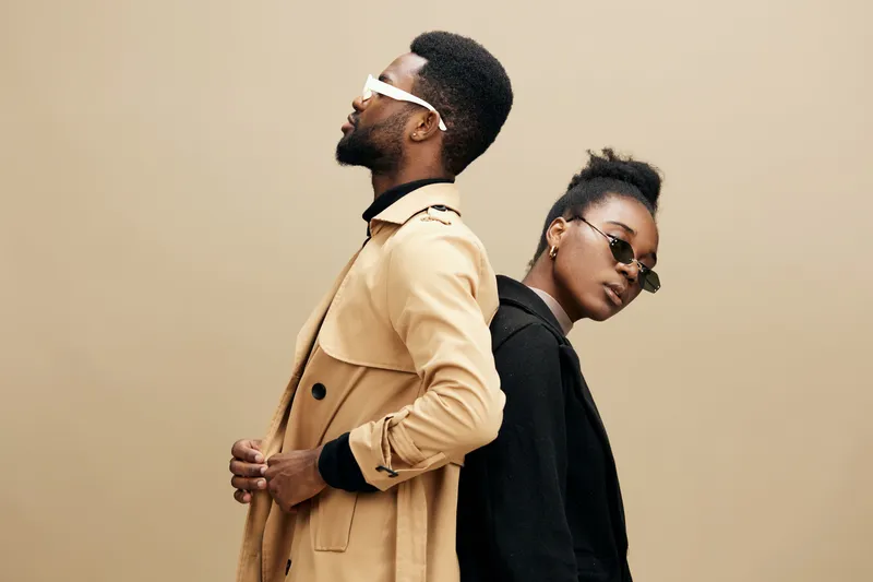 Stylish couple posing back to back, showcasing contemporary fashion with neutral tones and sunglasses, exuding confidence and modern elegance
