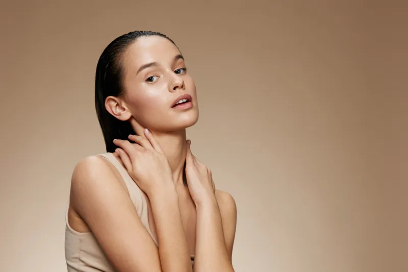Young woman with natural makeup poses gracefully against a neutral background, showcasing confidence and beauty in a minimalist style