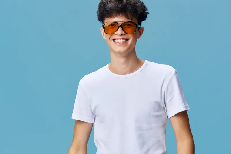 smiling young man wearing orange sunglasses and white t-shirt against blue background, cheerful and casual style with bright colors and clear lighting