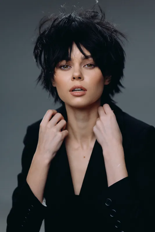 stylish woman with short black hair posing confidently in black jacket with dark gray background