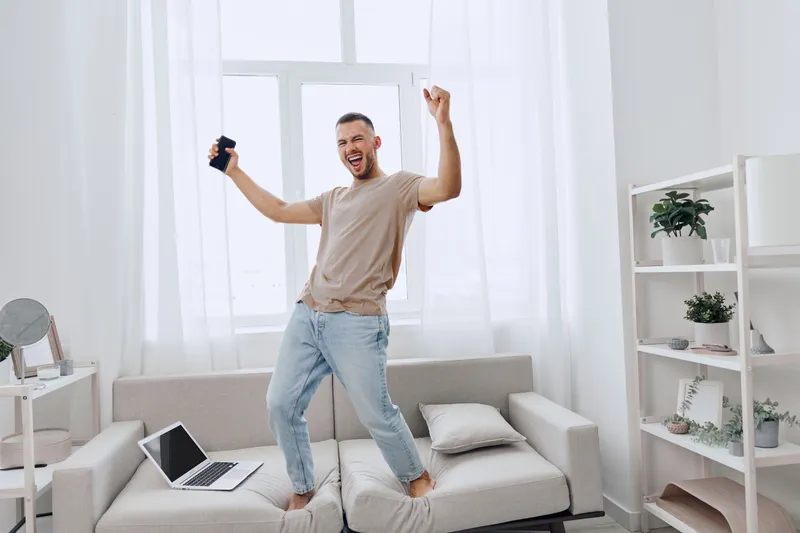 Joyful man dancing at home, celebrating personal freedom and digital detox while embracing emotional minimalism and soft masculinity in modern life.