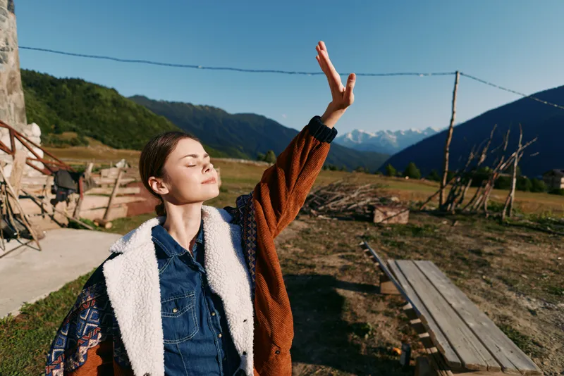 woman nature mountains sunlight outdoors portrait rural freedom enjoying fresh air with closed eyes and raised hand on a sunny day at a country farmhouse landscape for relaxation and wellbeing