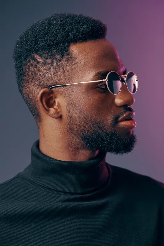 Stylish young African man wearing sunglasses and a black turtleneck, exuding confidence against a colorful gradient background