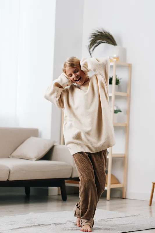 authentic moment of play at home, a dancer in a cozy sweater moves freely, capturing genuine comfort and spontaneous joy in a simple living space.