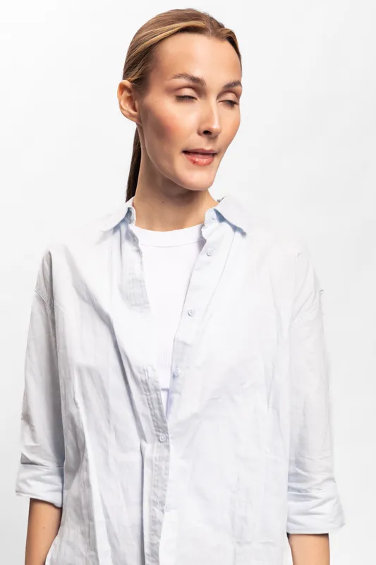 Young woman with light skin and tied hair wears white shirt and makes funny face with closed eyes and twisted mouth. Studio portrait on white background with casual style and humor concept.