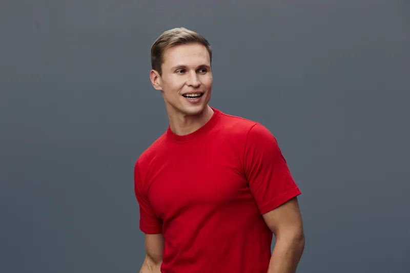 Full body smiling happy young man wearing red T-shirt and casual jeans pose against plain gray background studio portrait. Lifestyle, casual fashion, cheerful expression, positive vibe, casual style, 