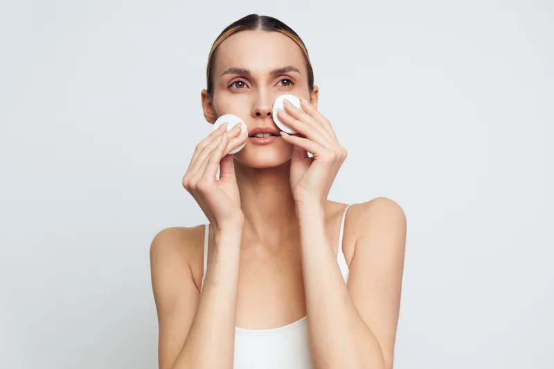 Focused woman cleanses her face with cotton pads, performing a gentle skincare routine. A calm moment of beauty, makeup removal, and hydration in a minimalist setting.