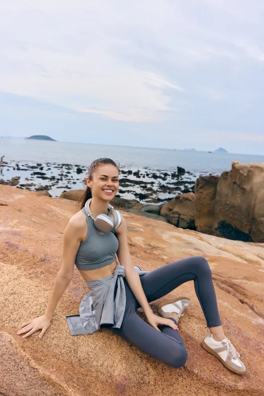 Young woman in activewear enjoying the seaside on a rocky beach, showcasing a healthy lifestyle and relaxation with ocean background, soft colors and serene vibes