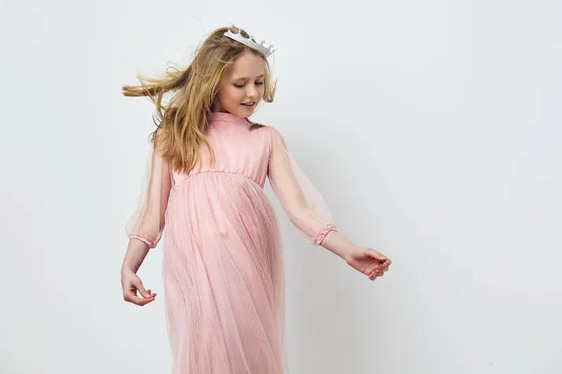 Young girl in a light pink dress, gracefully dancing against a minimalist white background, capturing joy and innocence in a modern style