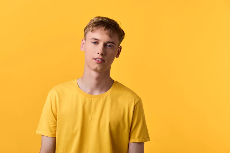 Young man wearing a yellow t shirt against a vivid yellow backdrop in a minimal studio, showcasing casual fashion, clean lines, and a calm, subtle expression. soft mood.