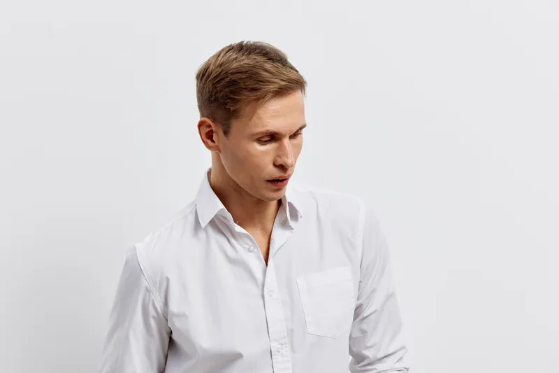 young caucasian man white shirt looking down thoughtful emotion isolated on plain background digital nomad concept work freelance